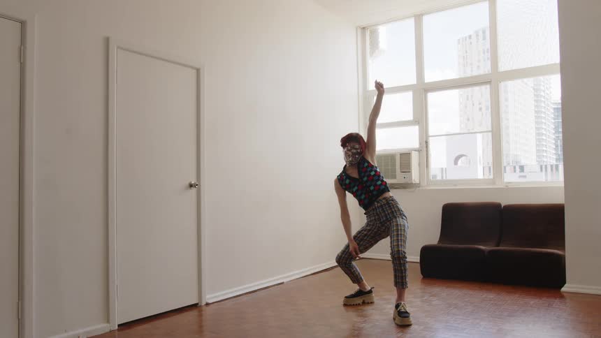 Woman dances while tilting her body and holding a telephone in an indoor space with a window in the background