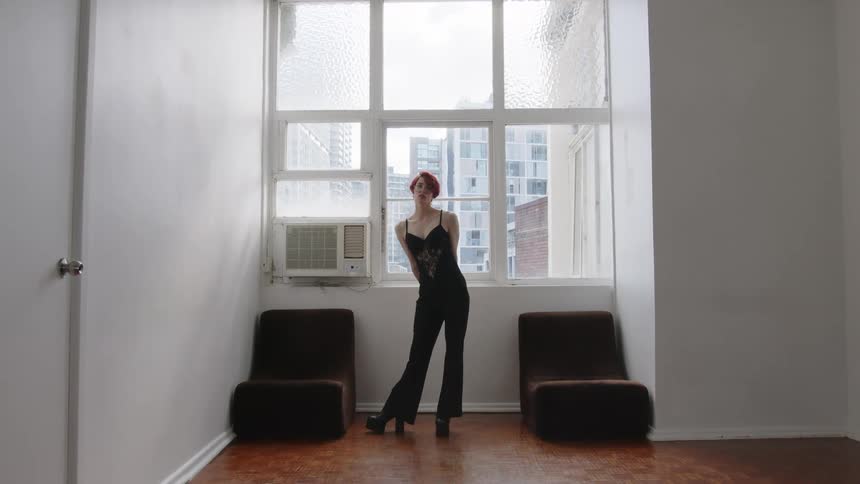 Woman standing in front of a window crosses her arms in an indoor space with buildings in the background