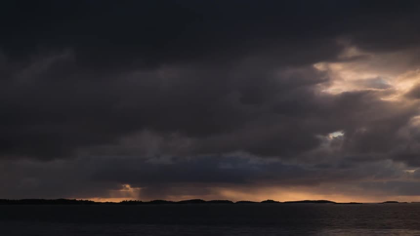 Dark stormy clouds flowing over ocean waters and mountains