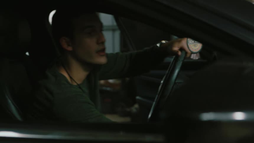Mechanic in a repair shop making a thumbs up gesture to a client sitting inside of a car who smiles and cheers indoors