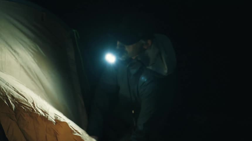 Tent in a dark environment illuminated by a handheld flashlight while a person stands in the background