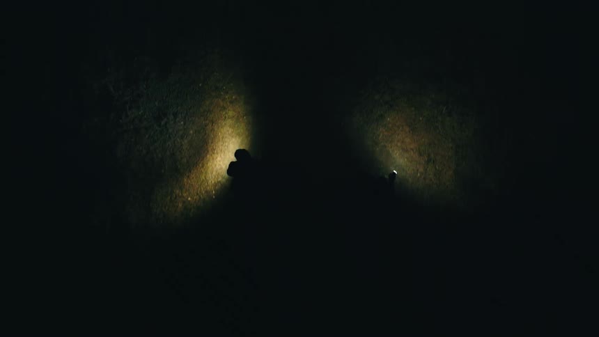 Silhouettes of two people cast on a wall by light beams in a dark environment