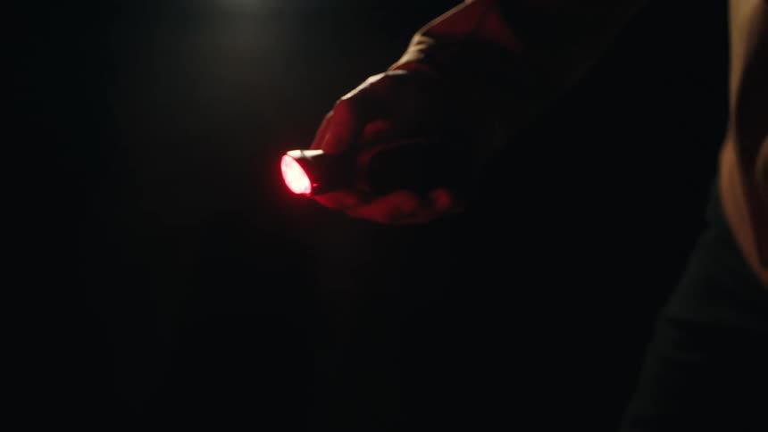 A person shown from the side is pressing a small light in the night