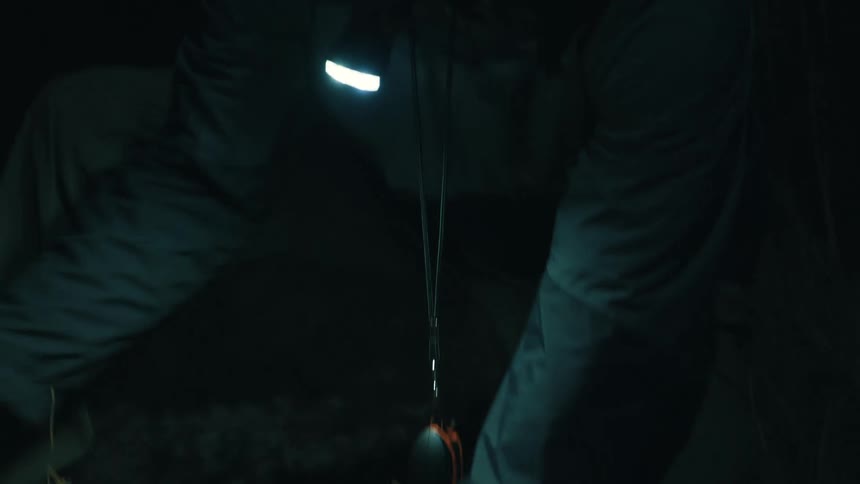 A man at night wearing a bright light on his head rushes while pushing on something in the ground