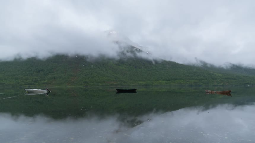 The fog rolls over the hill with three boats in water