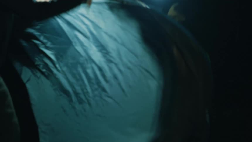 Two men set up a dark green pop up tent at a campsite during the night while using headlamps for illumination