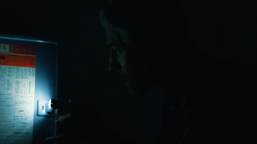 Adult man in a dark room using a flashlight to inspect a circuit breaker indoors during night time