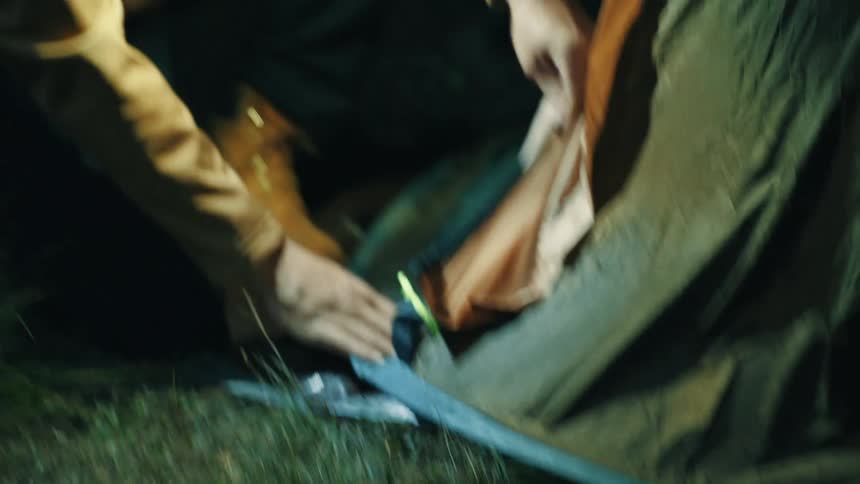 A man wearing a flashlight on his head is adjusting a tent at night
