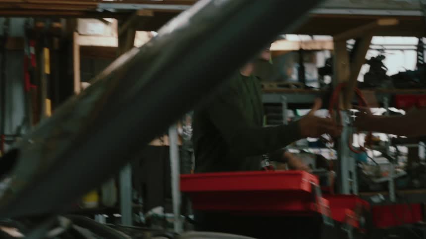 Man gets out of his car in a repair shop greets his colleague and together they examine a vehicles engine