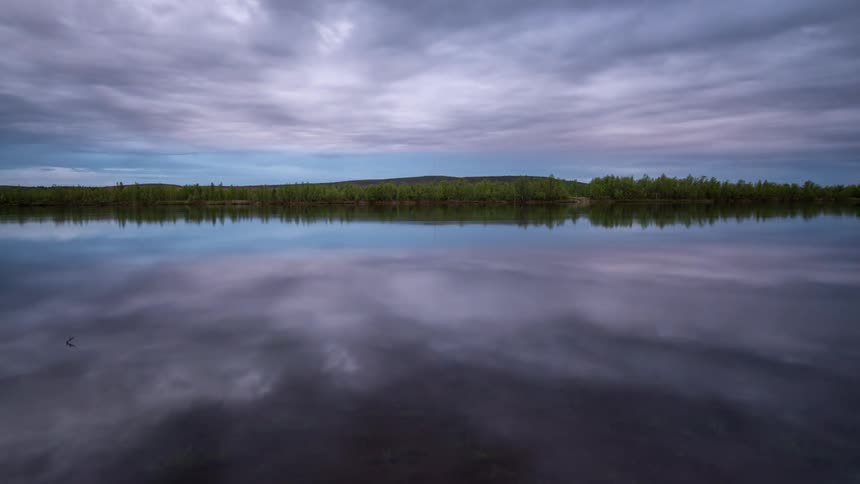 Clouds flowing through sky mirrored over lake