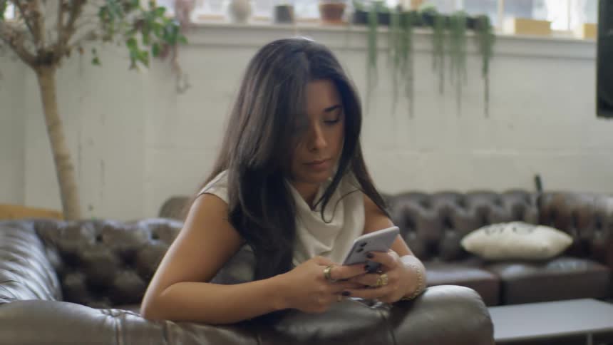 Woman sits in the living room during the day texting on her smartphone
