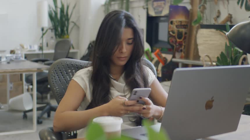 A woman using a phone and laptop at a desk