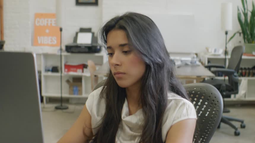 Young woman sits at a table typing on a laptop computer