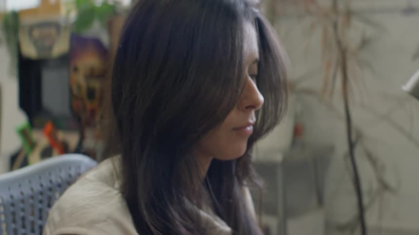 A woman with long dark hair wearing a light colored shirt sits at a desk in a professional office environment while working on a computer