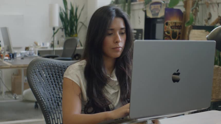 Woman sits in an office during the daytime while typing on her apple laptop
