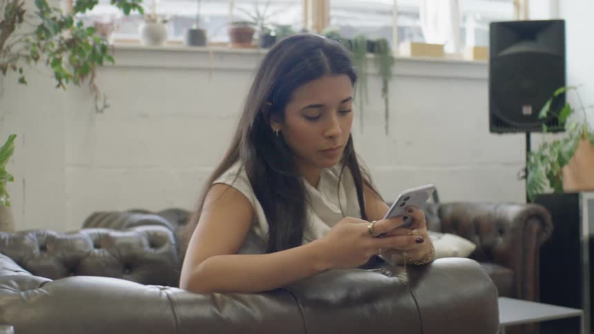 The woman sits on the couch and texts on her phone