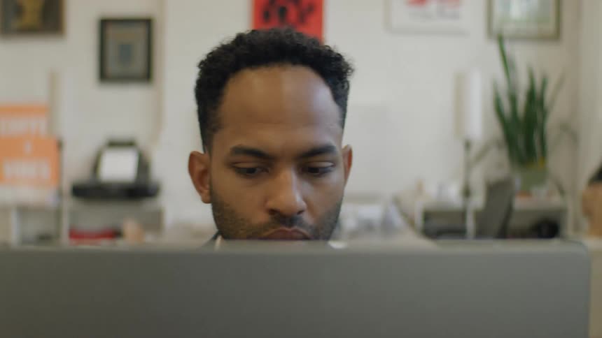 A man with short dark hair working at a laptop in a professional office environment