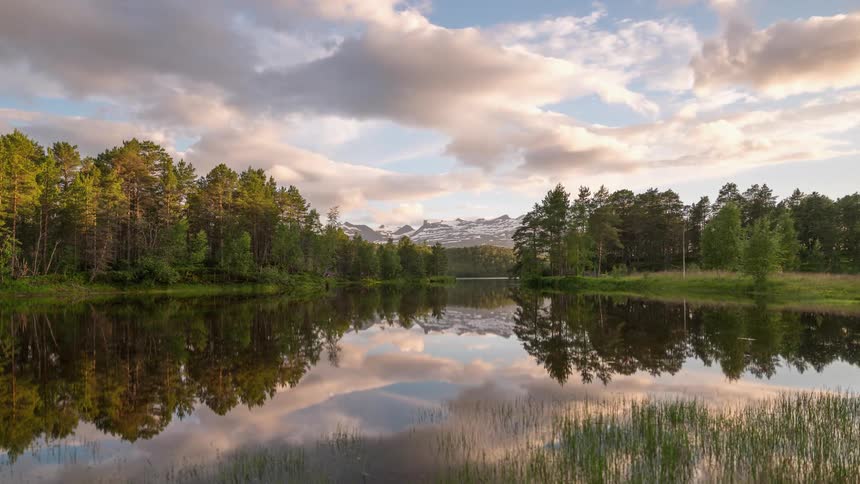 Clouds forming and flowing over forest lake and mountains