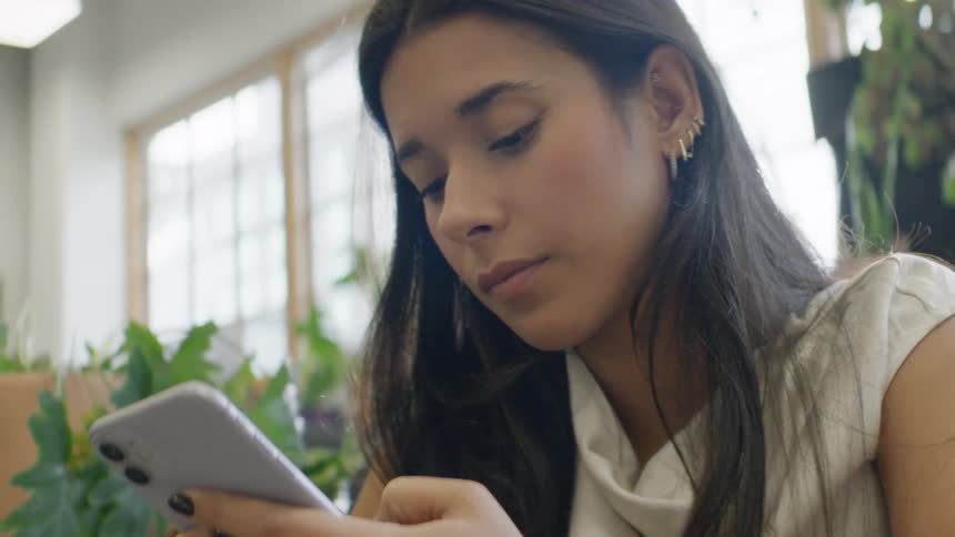 Woman using a smartphone indoors with plants and windows in the background