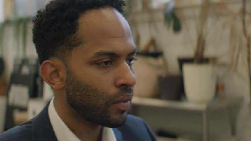 Man in profile wearing a suit in an office with plants and furniture in the background