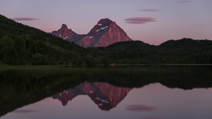 Purple sunset and still water by a forest and mountain peak