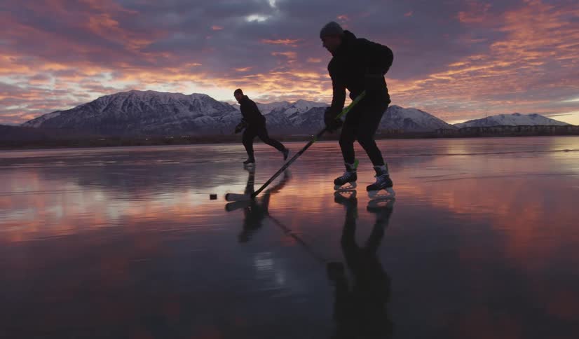 Two young men playing ice hockey with mountains along the frozen coast