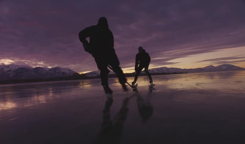 Two man play ice hockey on a vast frozen lake during a purple sunset