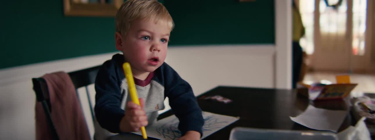 Girl looking at a book as her little brother picks out a marker to color his picture and their mother leaves the room