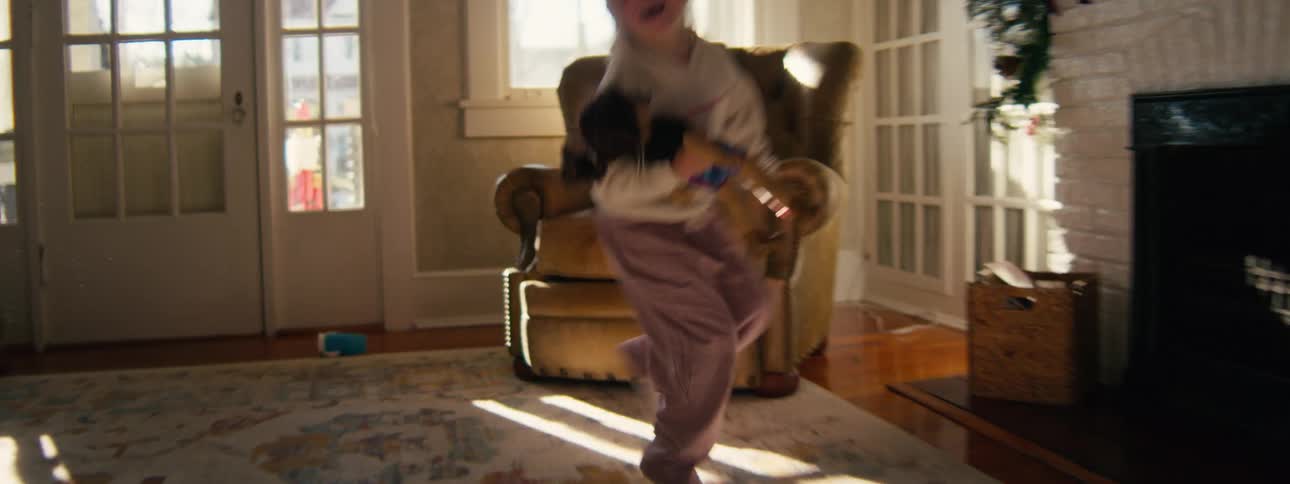 A young girl jumps and plays joyfully inside a sunlit living room