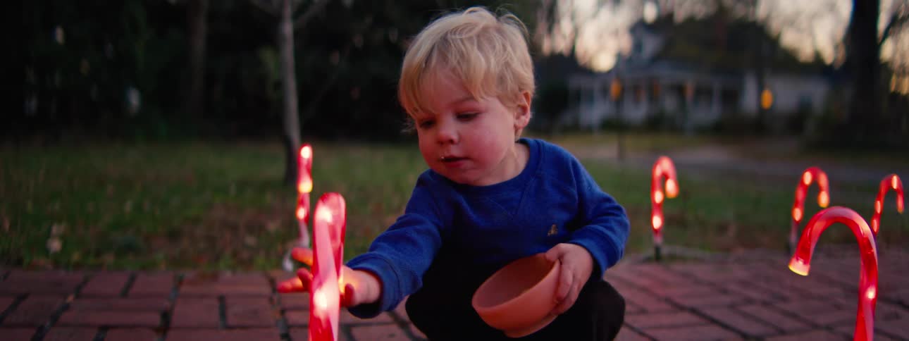 A toddler and a young girl play with a christmas decoration on a walkway at sunset the warm light shines on them as they enjoy the moment together