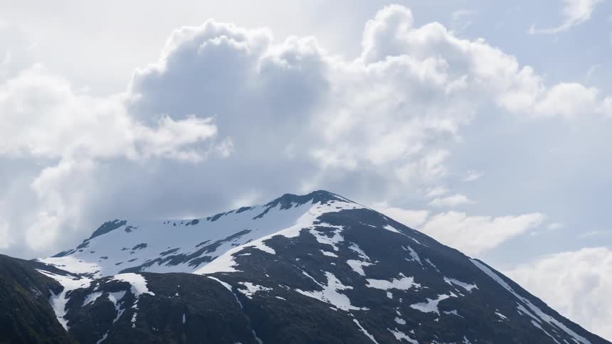 Clouds float in timelapse over a snowy mountain peak