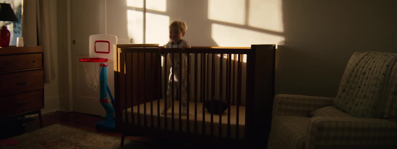 Child standing inside a wooden crib illuminated by sunlight entering through the bedroom window