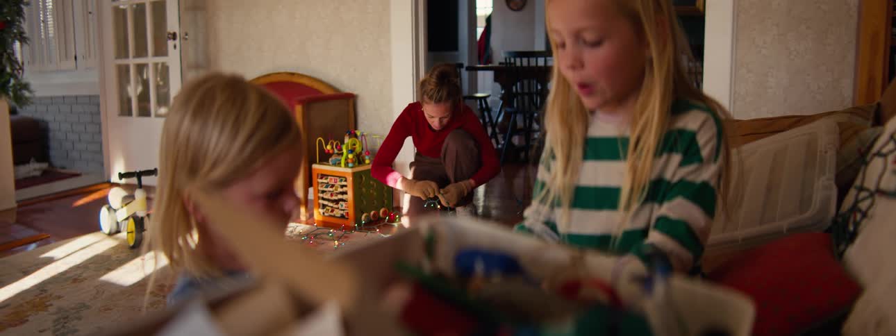Two girls playing as their mother fixes a string of christmas lights
