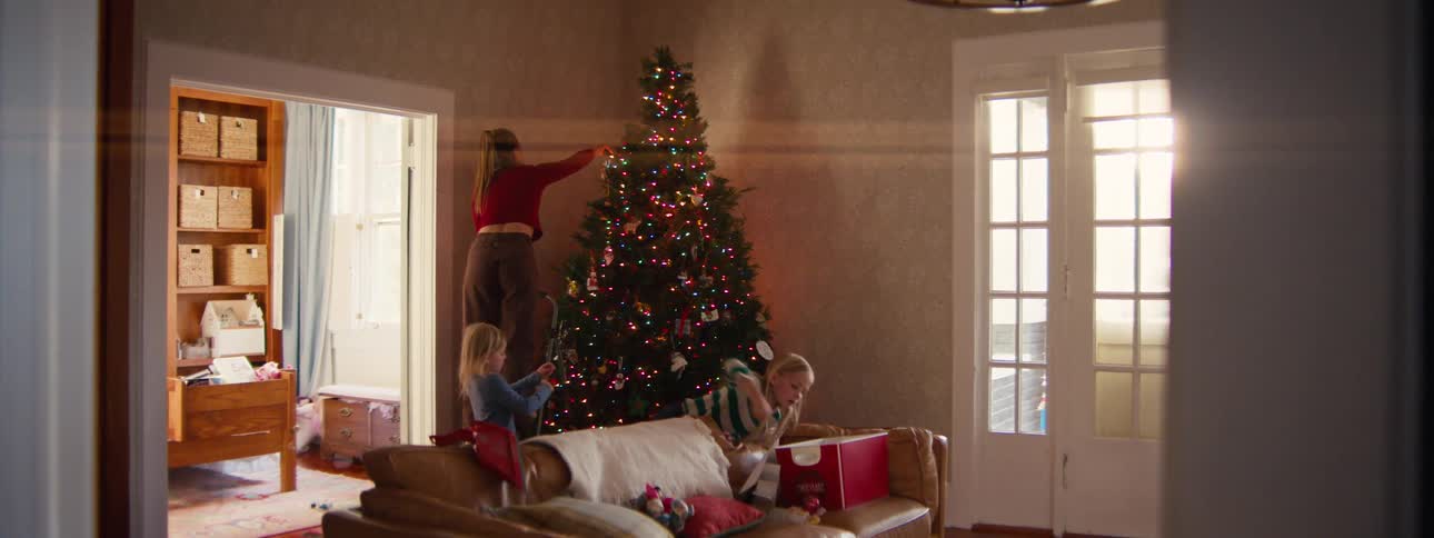 A woman and her children place ornaments on a decorated christmas tree