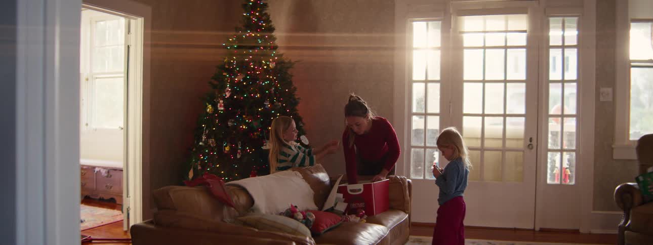 Two little girls and their mother taking christmas decorations out of a box and putting them on the christmas tree