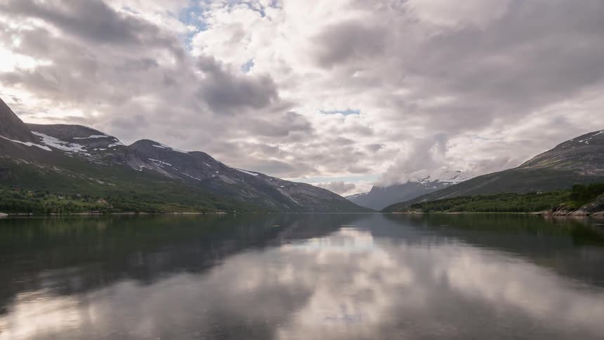 Clouds pass by above a reflective fjord in Norway