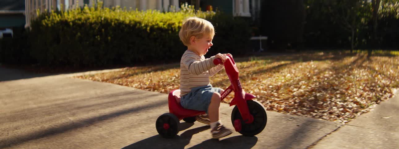 A child riding a tricycle outdoors on a sunny day
