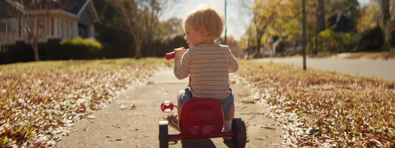 Little boy riding his small tricycle on a neighborhood sidewalk