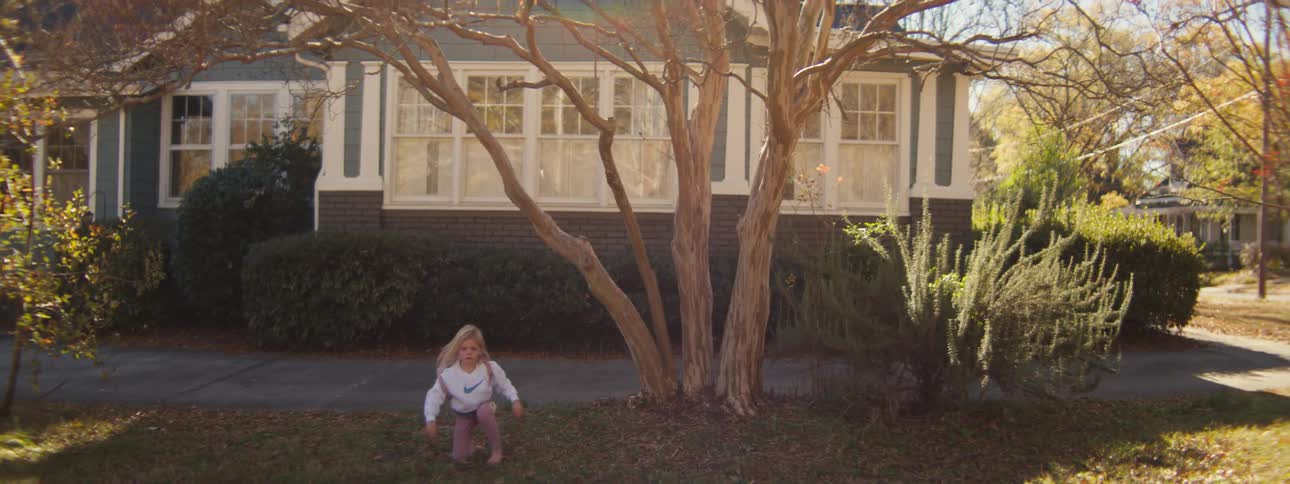A young girl jumps down after climbing a tree outside of a house