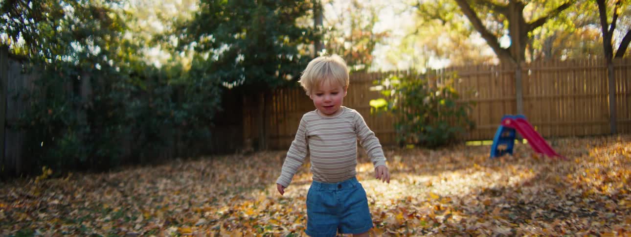 Little boy playing in his back yard throwing leaves and laughing