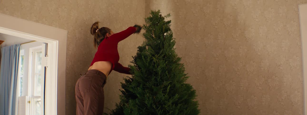 Woman placing string lights on a christmas tree inside an indoor space