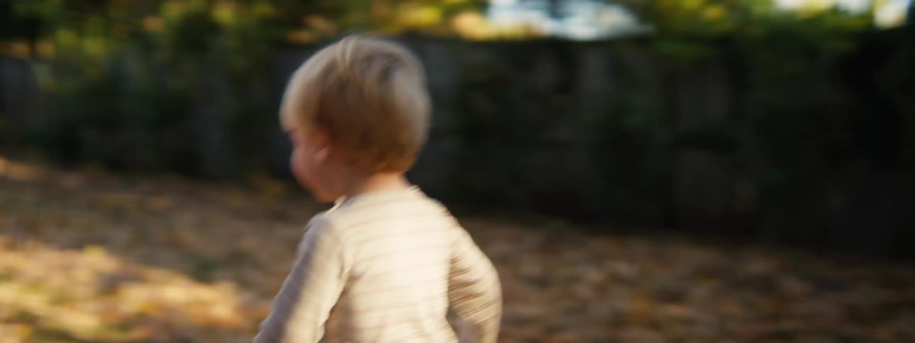 A young boy happily runs and plays across a leaf covered backyard