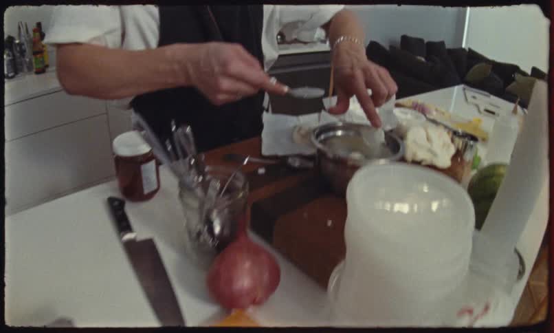 A person wearing an apron prepares food in a kitchen using a small spoon to portion out white cheese from a metal bowl