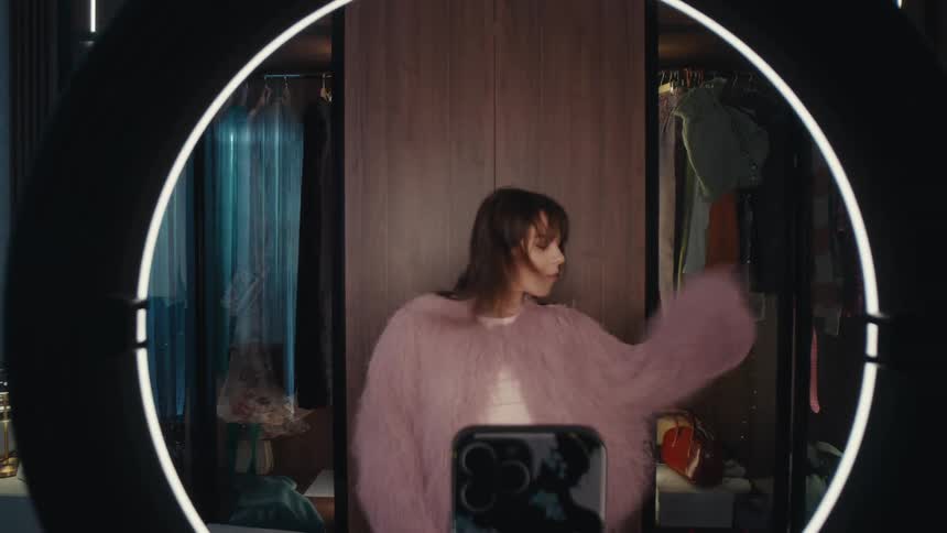 Woman dances in front of a phone on a tripod with a ring light in an indoor setting