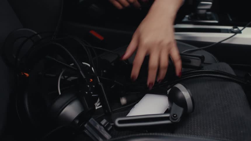 Young woman sitting in a car looks through her headphones and electronics on the seat