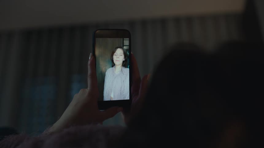 Person holds a phone while watching a video of a woman dancing indoors