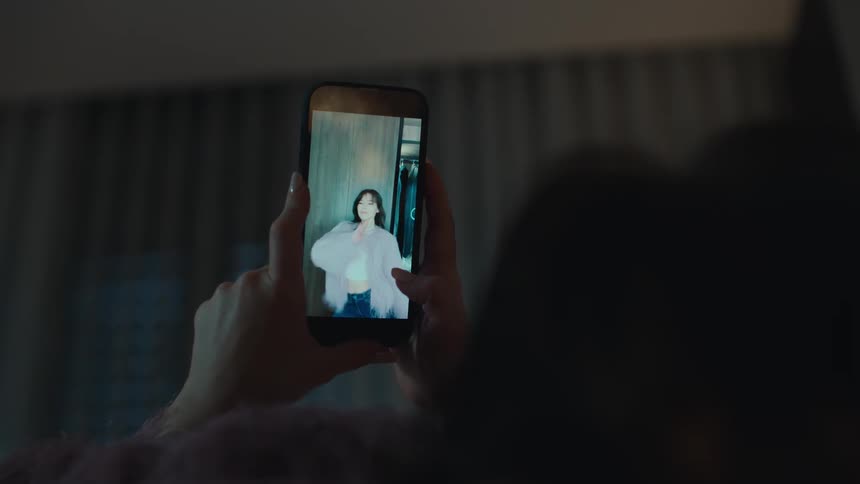 A woman laying down watches a woman dancing on their smart phone screen