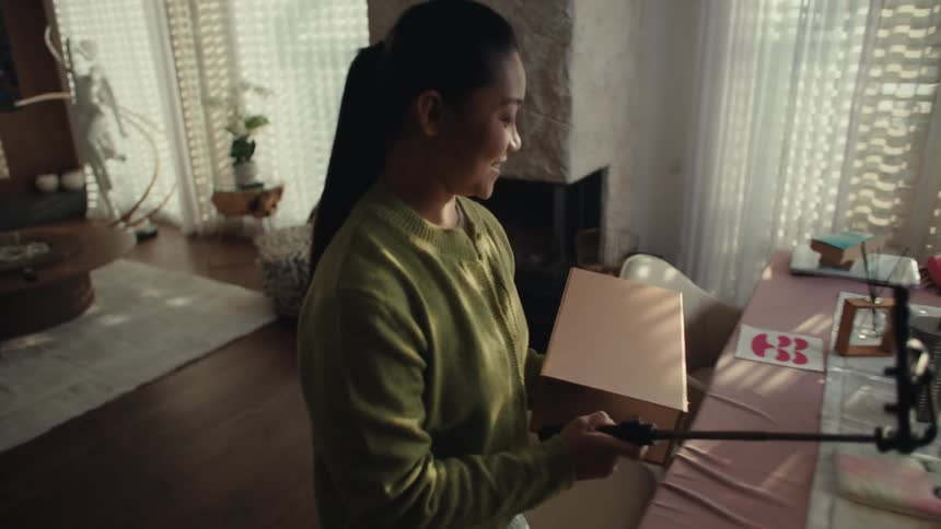 A woman is recording herself carrying a box inside of her home