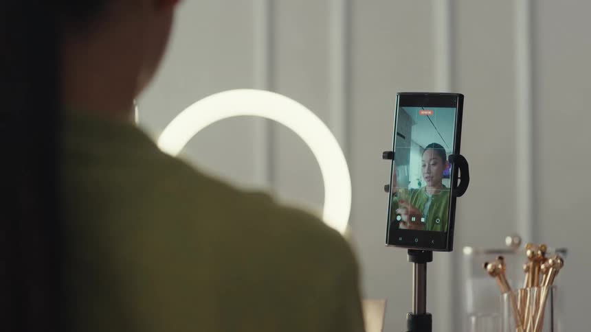 Woman records a video with a phone on a tripod and a ring light indoors