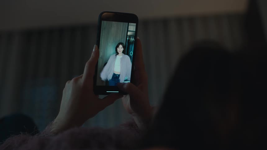 The woman is sliding through videos on her cell phone at home